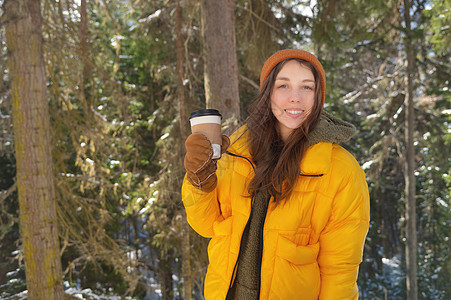 女孩在冬季森林喝热茶或咖啡 用纸杯微笑季节衣服假期女性雪花女士公园冻结杯子图片