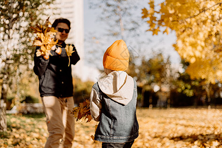 父亲和儿子在落叶的秋天公园里玩得开心 吐出叶子 小男孩和他爸爸在户外玩枫叶投掷自由情感家庭太阳喜悦乐趣孩子们孩子森林图片