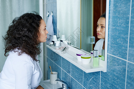 穿着白色浴袍的近身美女35岁 站在浴室里 反射在镜子中 想着她的外貌图片
