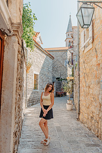 在一个美丽的夏日 在黑山布德瓦老城区的地中海中世纪城市 女游客穿过古老的狭窄街道 年轻美丽开朗的女人走在热带小镇的老街上 漂亮的图片
