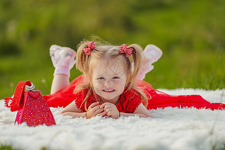 穿红裙子的女孩躺在白毯子上花园孩子们场地说谎太阳技术快乐工具婴儿公园图片