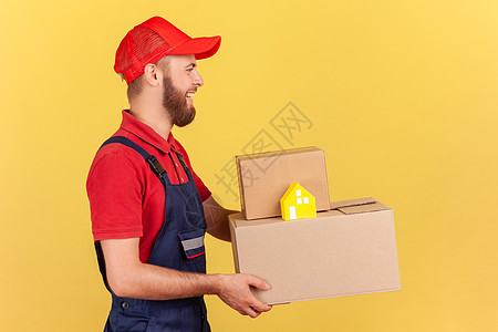 身着制服和红色帽子的送货员 手持纸板箱和纸房 门到门交货图片