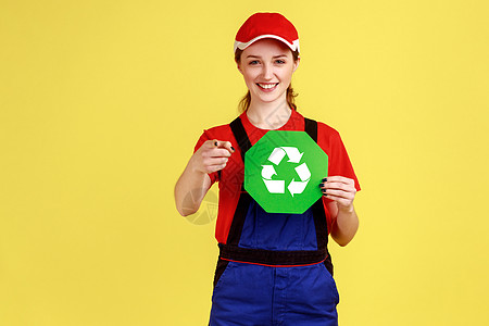 满意的女工站着 拿着回收标志 思考绿色 对着镜头看图片
