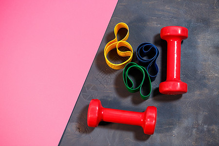 红色哑铃和松紧带 用于粉红色背景的运动 健康的生活方式 重量训练的健身器材 肌肉发育和健身训练瓶子瑜伽橡皮乐队力量女孩活动横幅身图片
