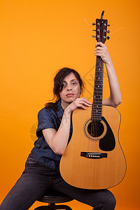 美丽的年轻歌手的肖像 在黄色背景的演播室里 拿着她的震荡吉他乐器女性女士歌曲唱歌乐趣生活艺术成人音乐图片