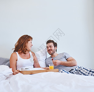 边吃早餐边甜言蜜语 一对夫妇在家里一起躺在床上享用早餐图片