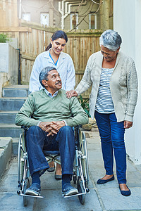 你去哪儿 我们就去哪儿 一位坐在轮椅上的开朗老人 白天在家中由妻子和一名女护士搀扶背景图片