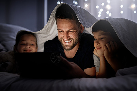 父亲和他的两个小孩晚上在床上一起使用数字平板电脑 他们每天晚上或白天都享受着娱乐的时光 (笑声)图片