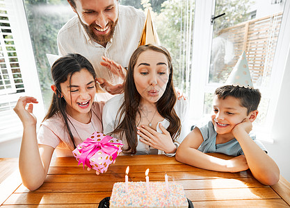 生日 家庭和庆祝活动 一位女士在她的蛋糕上吹蜡烛 丈夫和孩子宠爱妈妈 让她在她特殊的母亲节那天在家里开派对时感到快乐图片