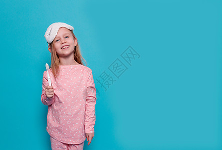 一个穿着睡衣和睡眠面具的小女孩 带着蓝色背景的牙刷图片