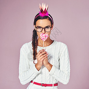 忘了那些甜言蜜语吧 一个年轻女人 用党冠和棒棒糖 在粉红背景上摆姿势图片