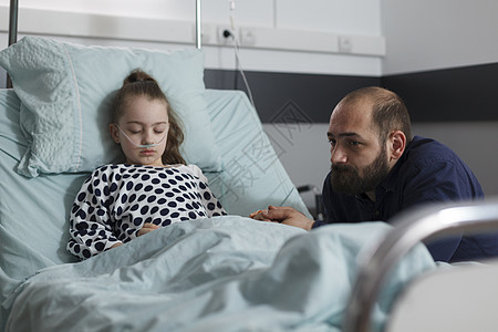 悲伤的父亲坐在住院的生病女孩旁边 躺在病人床上休息图片