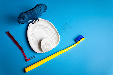 用于牙齿的无形牙套 透明牙齿对齐器 塑料牙套 用于矫直牙齿的保持器 牙刷和牙间刷在蓝色背景上 顶视图图片