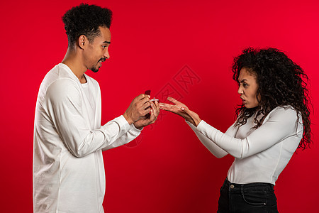 年轻的一对 非洲男人向他的情人女人求婚 她戴着红色工作室背景的戒指 但失望的心烦意乱的女孩不喜欢礼物图片