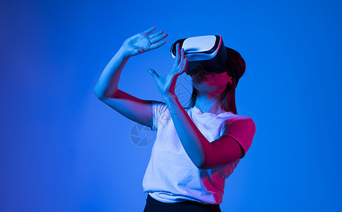 在工作室探索人工计算机世界或在霓虹灯下玩电子游戏的虚拟现实体验中 戴着 VR 耳机的黑发年轻女性兴奋地触摸着空气微笑娱乐头盔创新图片