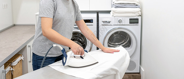 在洗衣房熨烫白衬衫 背景是洗衣机木板器具女士烘干成人衣服洗衣店房间衣板家庭主妇图片