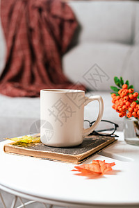 静物书 蜡烛 罗文浆果和一杯茶或咖啡放在客厅的桌子上 家居装饰在舒适的房子里 秋季周末概念 毯子和格子花呢 落叶和家居装饰早餐公图片