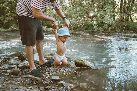 爸爸把他的小宝宝抱在河边 有趣的儿子绑着他的腿不想在水里游泳了图片