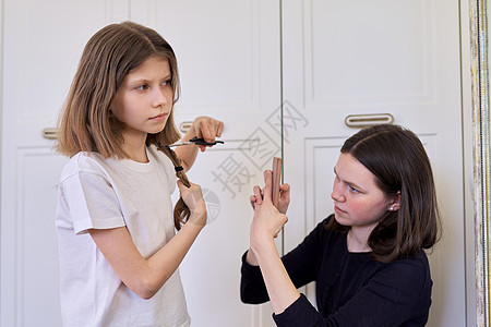 女孩用剪剪刀割自己的头发 姐姐大姐少女在智能手机上制作视频图片