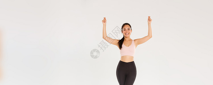 全长苗条健康的亚洲微笑女孩锻炼 穿着运动服 举起手 好像拿着标语或横幅 宣传运动器材或健身房会员折扣福利教练讲师身体训练肌肉跑步图片