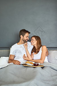 一对快乐的年轻夫妇在家里一起在床上吃早饭 起床后又发光 喝着葡萄酒和美食图片