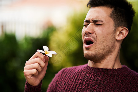 过敏季节让他打喷嚏 一个年轻人闻到一朵花的味道后又打喷嚏图片