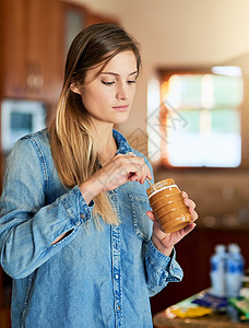 一个年轻女人用勺子从罐子里吃花生酱 来尝尝甜美的滋味图片