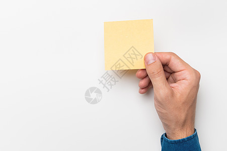 一个穿着牛仔衬衫的男人的手拿着一张文具贴纸 用于在白色背景上书写 空白纸空白提醒待办事项列表 办公用品注释消息 办公室和商业概念图片