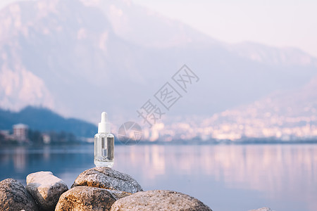 护肤场景透明质酸 石头上的血清护肤玻璃瓶 山湖背景 含有肽和胶原蛋白的血清产品化妆品 现代品牌化妆品包装的影子背景