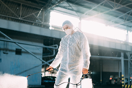 检疫期间穿着白色防护服的男子喷洒表面抗菌消毒剂喷雾器面具背光危害男人民众环卫工人工作服清洁工疾病防护图片
