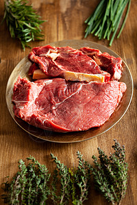 在绿色蔬菜和木制桌上草药旁边的旧板上 有不同类型的红色肉类图片