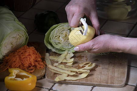 一名妇女以新鲜蔬菜为背景 在厨房里剥土豆皮骰子女士美食土豆收成盘子木头营养烹饪木板图片