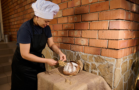 妇女面包师将小麦小麦的小点贴在新鲜烘烤的全谷物面包旁边 放在桌布上图片