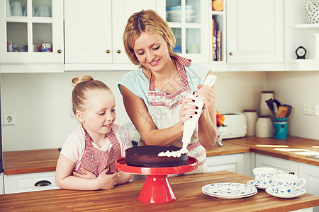 小心地锦上添花 可爱的小女孩和她妈妈在厨房里给蛋糕抹糖霜背景