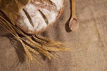 一整片谷物面包 包括面粉 小麦小块子和一勺木汤匙 布在麻袋桌布上图片