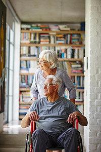 年长时配偶支助 一名高级妇女在坐在轮椅上的丈夫身后站立着图片