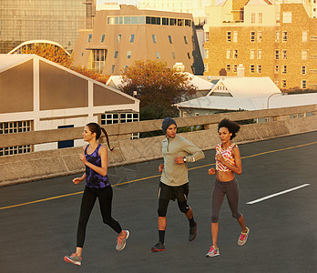 我们喜欢清晨的静悄悄跑步 早上有三名慢跑者冲下一条空高速公路背景图片