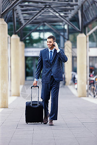上下班途中的商务沟通 一位英俊的年轻商务人士拿着他的行李走进机场时正在玩手机图片