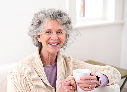 轻松的早晨……退休的好处 一位高级女士坐在沙发上端着一杯咖啡的画像图片