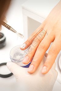 在美容院将丙烯粉涂在女性指甲上 加强钉子丙烯粉的强化剂化妆品沙龙工作温泉治疗产品女士手指抛光女孩图片