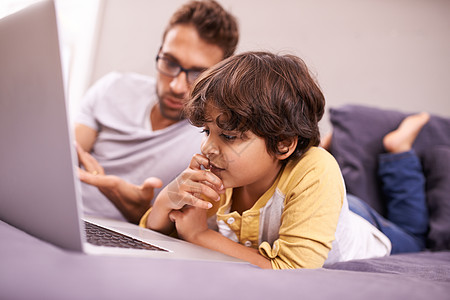 让我们玩猜谜游戏 父亲和儿子躺在床上时用笔记本电脑图片