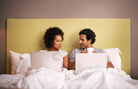 床上电脑一对年轻夫妇带着笔记本电脑在床上睡觉 他正在工作背景