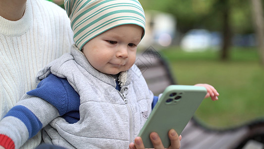 一个快乐的男婴的画像 在露天看手机上的卡通片 高兴地挥舞着双手图片