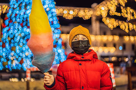 在冠状病毒 COVID 19 期间戴着面具在圣诞市场上拿着棉花糖的男孩 圣诞市场上快乐的孩子 圣诞节家庭的传统休闲流行棉布喜悦警图片