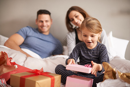 盛大的开张 一个小女孩在床上 从父母那里收到礼物的礼物图片