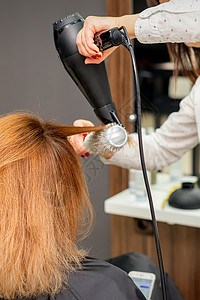 在美发工作室吹干头发 在美容院 女美发师造型师用吹风机和圆刷红头发吹干头发客户美容师梳子温泉护理发型服务理发师两个人工作图片