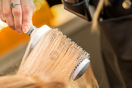 发型师亲手擦干金发 在美容院里用理发机和圆梳子烘干头发美容吹风机刷子造型师工作治疗理发师冰壶女士沙龙图片