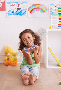 微笑的小女孩学习的基石 一个可爱的小女孩在玩字母表块游戏 你觉得呢?背景