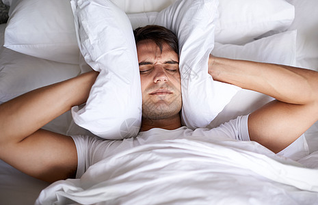 所有的噪音是怎么回事 一个年轻人在试图睡觉时用枕头捂住耳朵图片