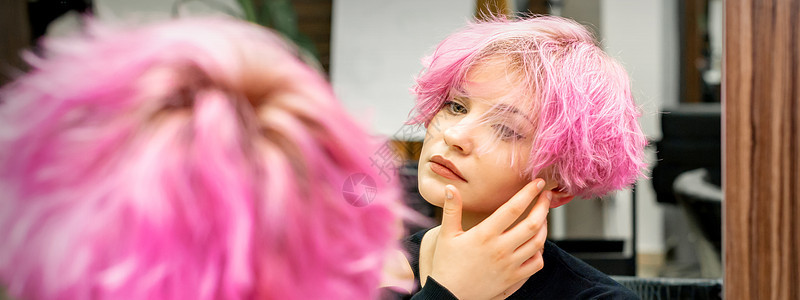美丽的年轻白种女人 留着新的粉红色短发型 在美发沙龙的镜子里看着自己的倒影 检查发型卷曲魅力头发女士化妆品女孩染料反射梳妆台成人图片